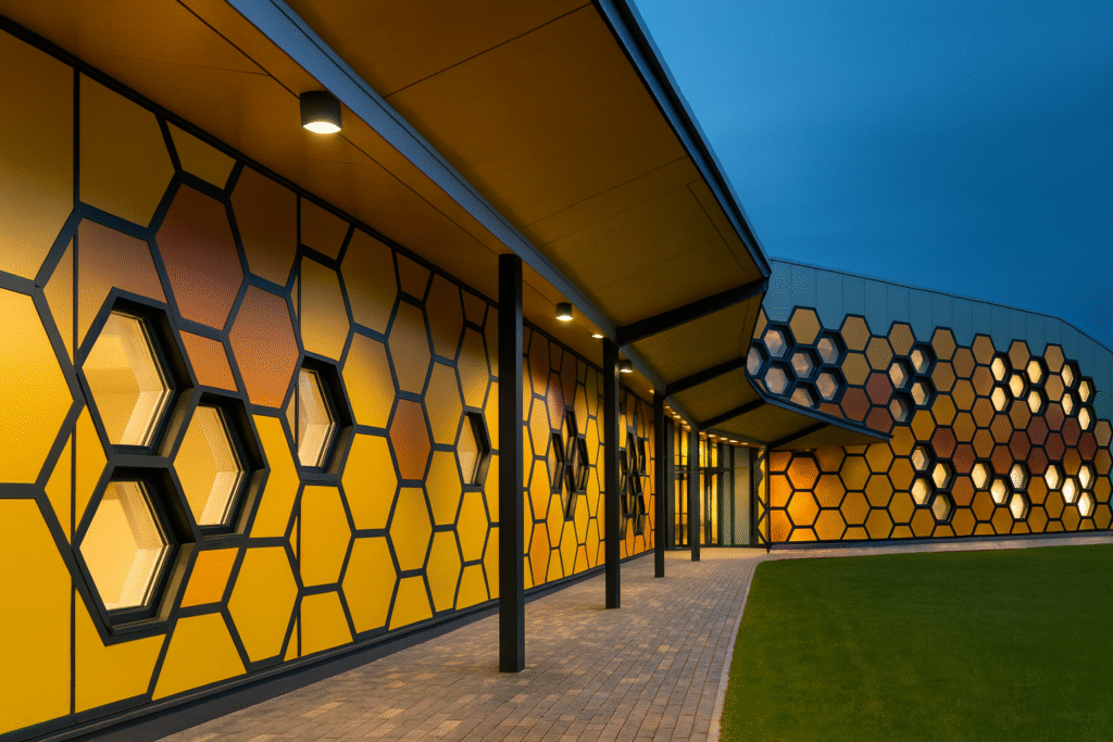 Fachada con módulos hexagonales de PVC curvado y estructura metálica, iluminación perimetral al atardecer.